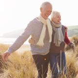 Senior Couple Walking Through Sand Dunes On Winter Beach Smiling